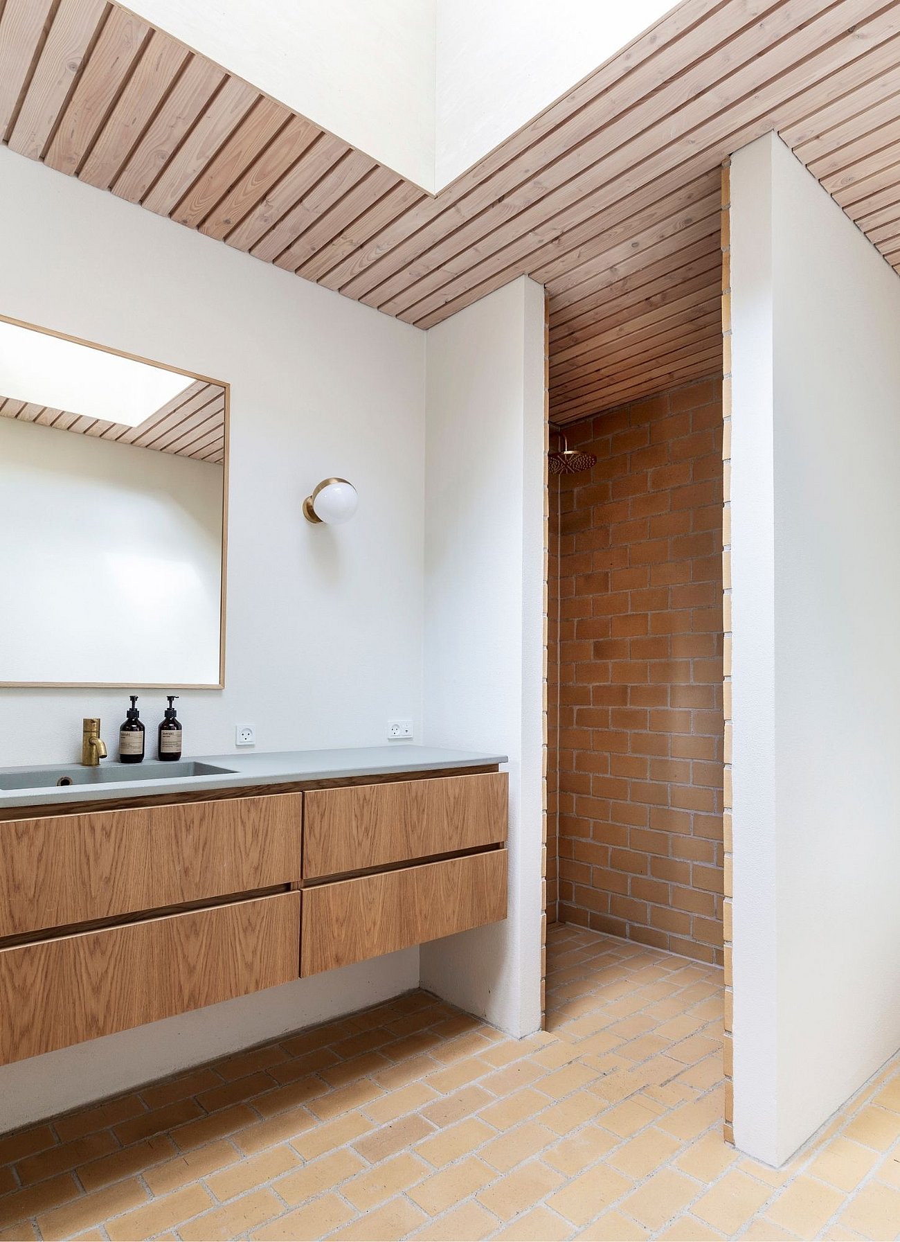 70'er inspireret badeværelse med gulvbelægning og bruseniche i gule mursten og træbeklædt loft