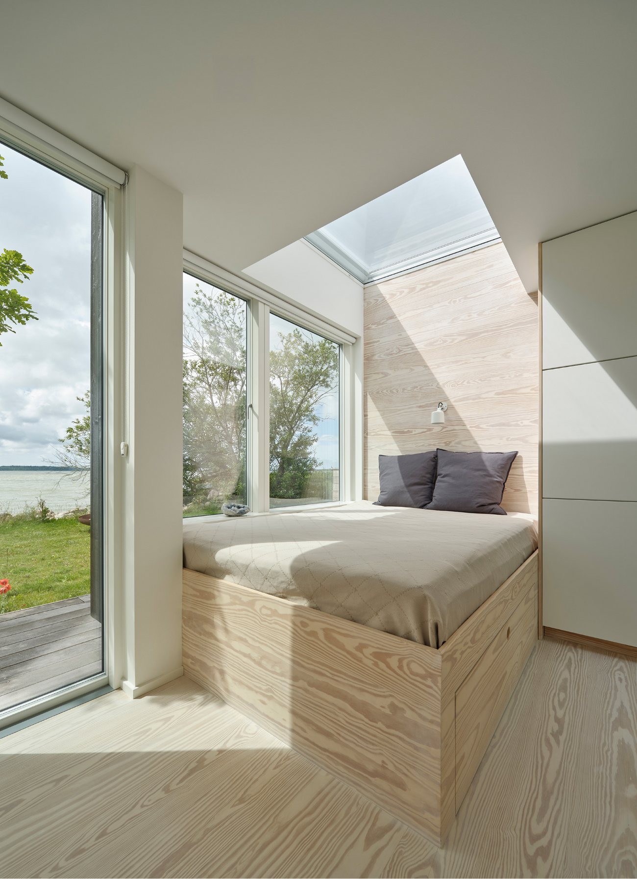 Lyst soveværelse i sommerhus med ovenlysvinduer og udsigt til sø