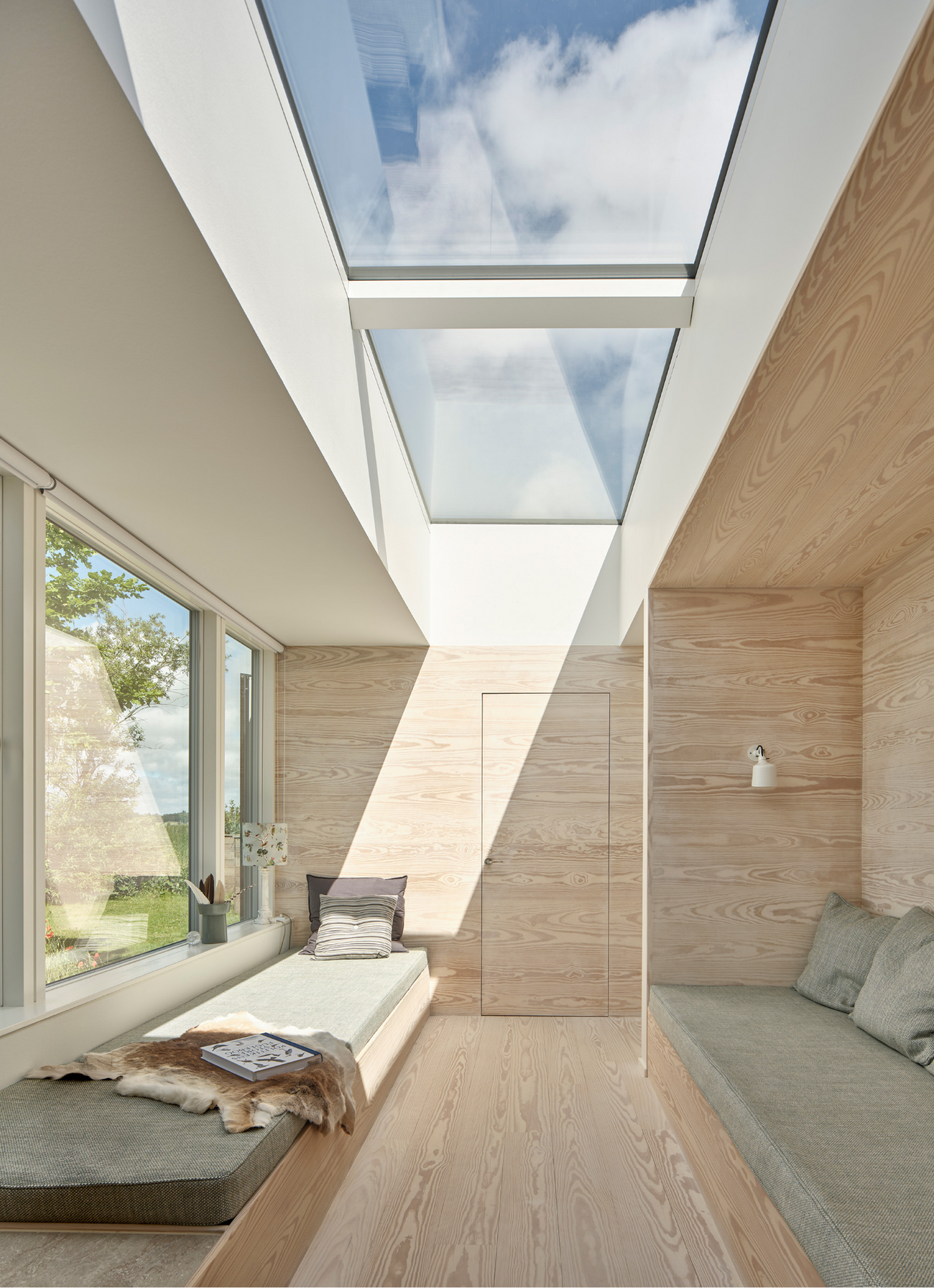 Lys stue i sommerhus med ovenlysvinduer og udsigt til sø