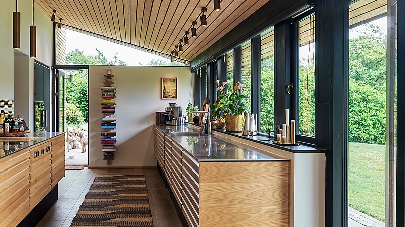 Udvendige eksisterende underbeklædning af træ har været afsæt for nyt loft og eksisterende køkken er renoveret.

Forbindelse til have og  indretningsmuligheder er styrket, mens sansevækkende naturmaterialer samler sig i en ny atmosfærefyldt helhed.
